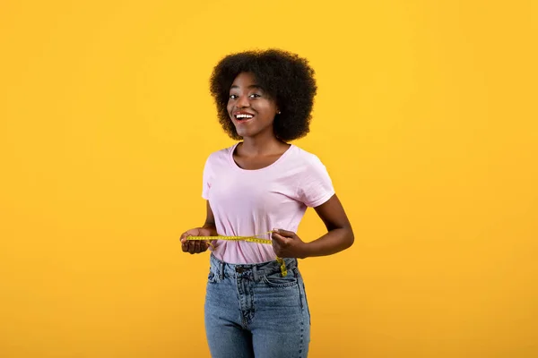 Gewichtsverlust Konzept. Fit afrikanisch-amerikanische Dame misst ihre Taille mit Klebeband über gelbem Studiohintergrund — Stockfoto