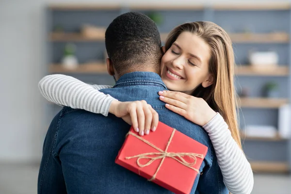 Romantisch geschenk. Dankbare vriendin knuffelen haar zwarte vriendje en vasthouden huidige doos — Stockfoto