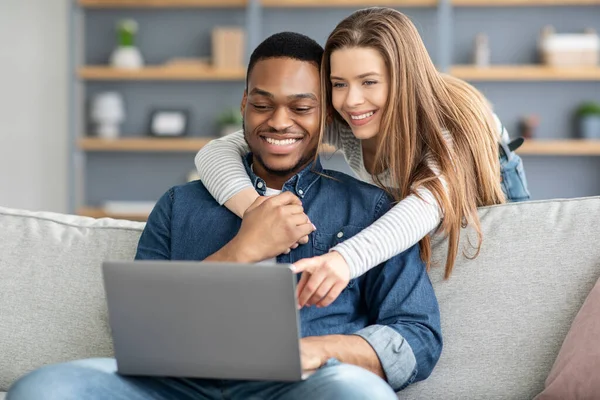 Casal Interracial feliz usando laptop, relaxando em casa juntos — Fotografia de Stock