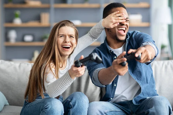 Alegre pareja multicultural divirtiéndose en casa, jugando videojuegos juntos —  Fotos de Stock