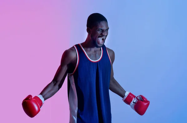 Агресивний чорний спортсмен в боксерських рукавичках кричить в гніві на неонове світло. Концепція бойового спорту — стокове фото