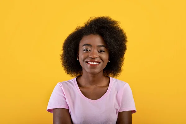 Persona feliz. Retrato de mujer negra amigable con el pelo rizado mirando a la cámara y sonriendo, posando sobre fondo amarillo — Foto de Stock