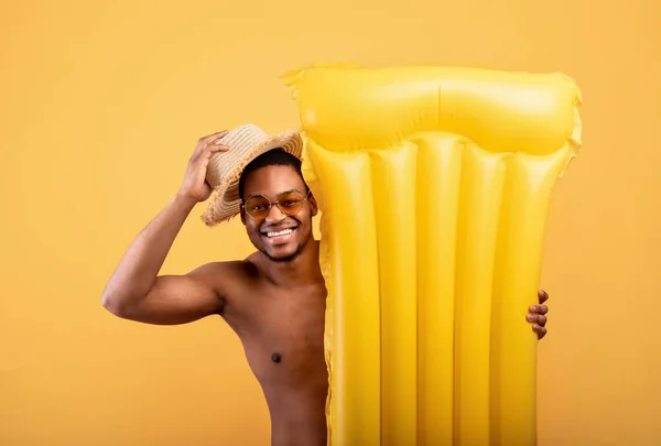 Hola verano. Hombre negro levantando su sombrero de paja en gesto de saludo, escondido detrás de lilo inflable sobre fondo amarillo —  Fotos de Stock