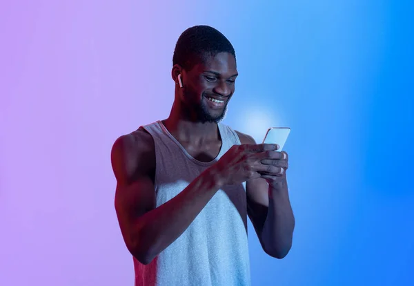 Orang Afrika-Amerika yang menarik dengan ponsel memakai earphone, memetik daftar lagu dalam cahaya neon — Stok Foto