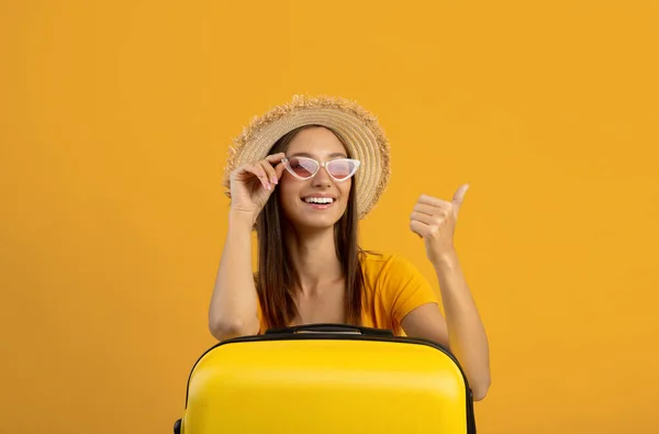 Mujer alegre en gafas de sol apoyada en la maleta, mostrando espacio para copiar — Foto de Stock