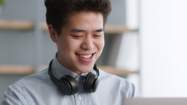 Close-up portret van gelukkige jonge aziatische man met oortjes in de nek chatten met vrienden, lezen bericht en lachen — Stockvideo
