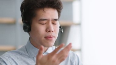 Çevrimiçi iletişim. Genç Asyalı destek servisi yöneticisi kulaklık takıyor müşteriyle konuşuyor, sistemi anlatıyor.