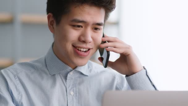 Jonge vriendelijke Aziatische man manager praten met partners via mobiele telefoon, genieten van deal, werken op afstand op kantoor — Stockvideo