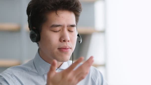 Online komunikace. Mladý asijský manažer podpůrných služeb nosí sluchátka mluvit s klientem, vysvětlující systém — Stock video