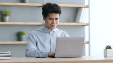 Genç Asyalı neşeli metin yazarı dizüstü bilgisayarda yazıyor, pazarlama stratejisi ya da iş planı oluşturuyor, ofiste çalışıyor.