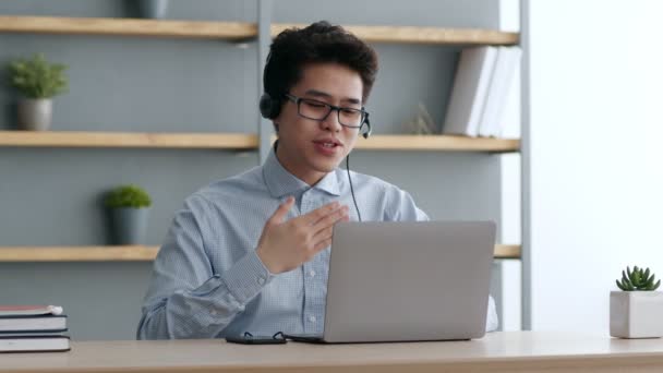 Positiv ung asiatisk kille i glasögon bär headset videokonferens med potentiell arbetsgivare via laptop — Stockvideo