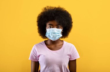 Enfeksiyon ve koruma konsepti. Sarı arka planda izole edilmiş tıbbi maske takan Afrikalı Amerikalı genç bir kadın.