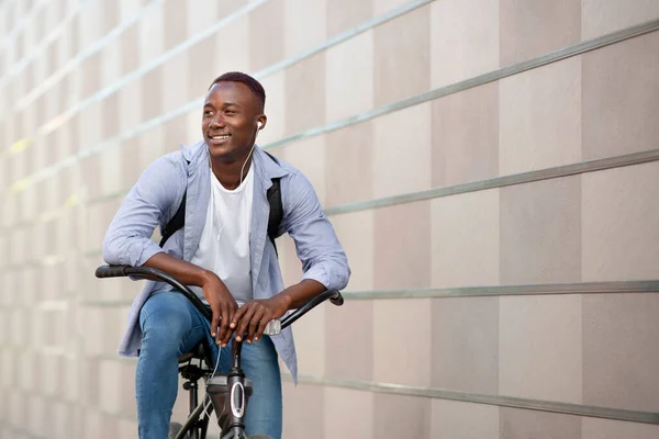 Feliz hombre afroamericano escuchando música mientras monta bicicleta cerca de la pared de ladrillo, espacio para el texto —  Fotos de Stock