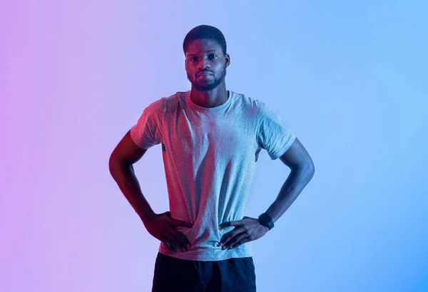 African American male fitness modell stående med armar på höfterna, tittar på kameran i neon belysning — Stockfoto