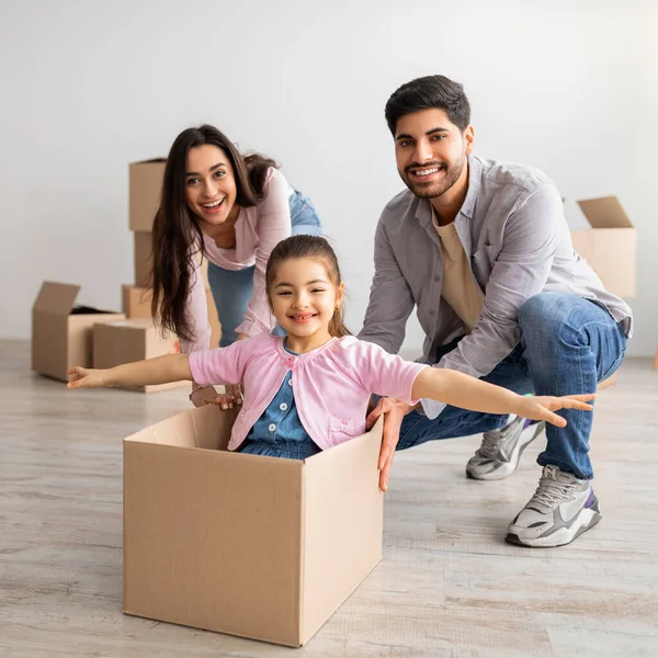 Concetto immobiliare. Gioiosa famiglia orientale divertendosi e festeggiando il giorno in movimento, i genitori cavalcano la figlia nella scatola — Foto Stock