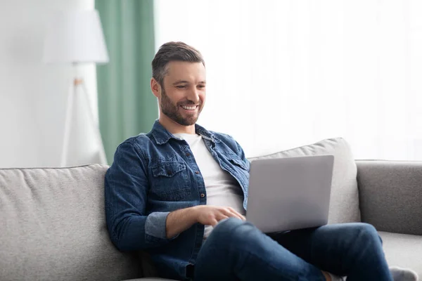 Sorrindo homem usando laptop, tendo trabalho a tempo parcial em casa — Fotografia de Stock