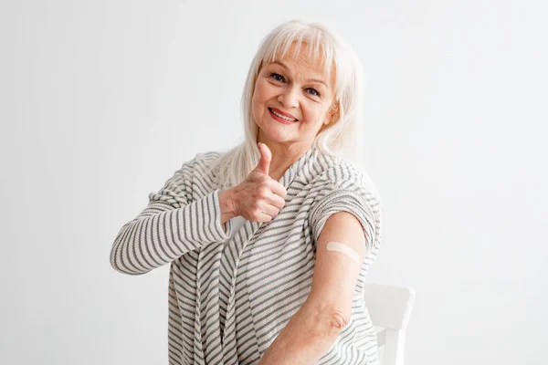 Felice vaccinato maturo donna gesturing pollice-up su sfondo bianco — Foto Stock