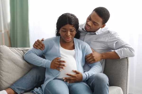 Terhes nő, akinek munkaerő fájdalom, ül a férj a kanapén — Stock Fotó
