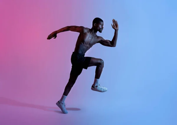 Comprimento total de atleta preto forte em sportswear correndo em luz de néon, vista lateral. Conceito de estilo de vida ativo — Fotografia de Stock