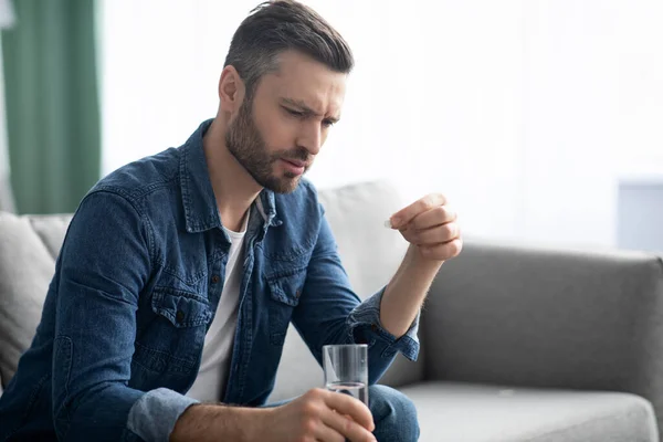 Homme barbu bouleversé avec un verre d'eau prenant des médicaments — Photo