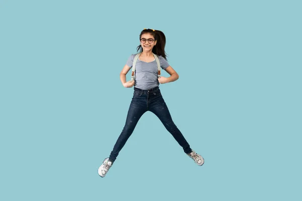 Ενθουσιασμένη έφηβη μαθήτρια με σακίδιο να πηδάει στον αέρα σε μπλε φόντο στούντιο — Φωτογραφία Αρχείου
