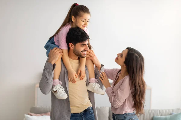 Família oriental se divertindo, jovem pai segurando a filhinha em seus ombros e sorrindo um para o outro — Fotografia de Stock