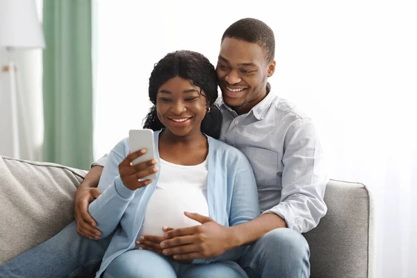 Alegre grávida casal afro-americano usando telefone celular — Fotografia de Stock