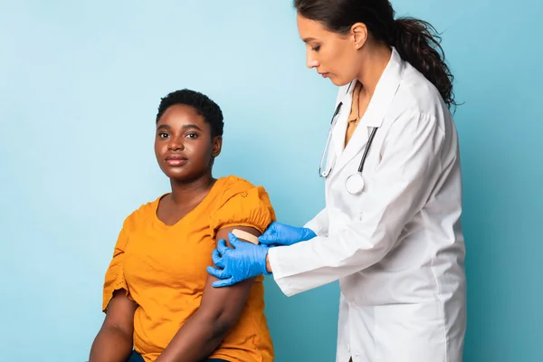 Doctor toepassen van gips strip op arm na injectie, blauwe achtergrond — Stockfoto