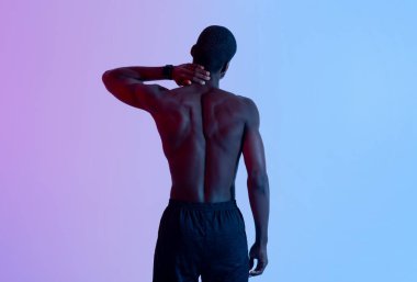 Çıplak gövdesiyle boynunu ovuşturan, neon ışıkta acı çeken genç siyahi sporcunun arkası.