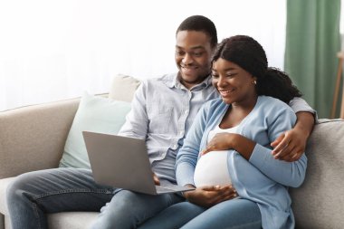 Hamile siyahi çifti sevmek evde dizüstü bilgisayar kullanmak, film izlemek.