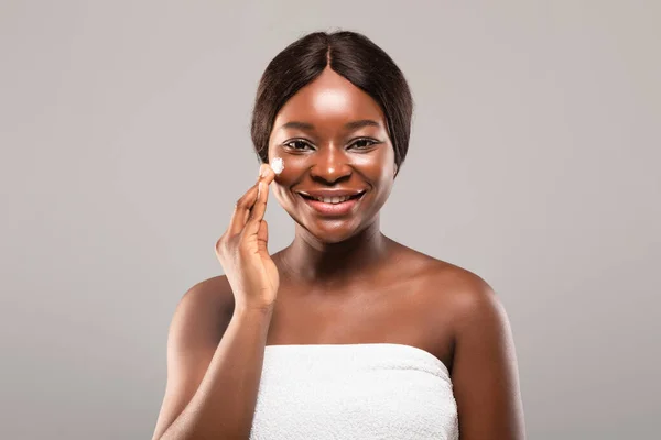 Hudvård koncept. Porträtt av attraktiv afroamerikansk kvinna Tillämpa Moisturising Cream — Stockfoto