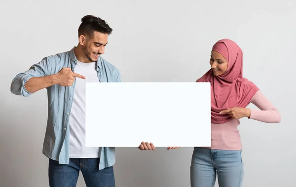 Glückliches islamisches Millennial-Paar hält und zeigt auf langes Blanko-Plakat — Stockfoto