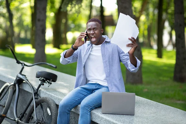 Irritado afro-americano homem com documentos gritando em celular perto de sua bicicleta no parque — Fotografia de Stock