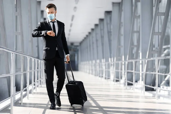 Empresário em máscara facial andando pelo terminal do aeroporto, verificando o tempo — Fotografia de Stock