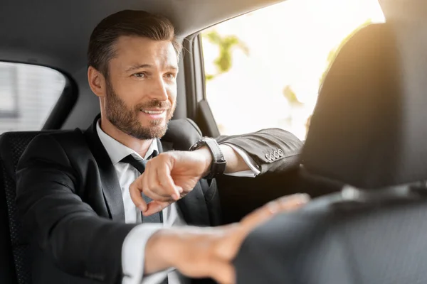 Snygg skäggig man i kostym sitter i taxi, kollar tiden — Stockfoto