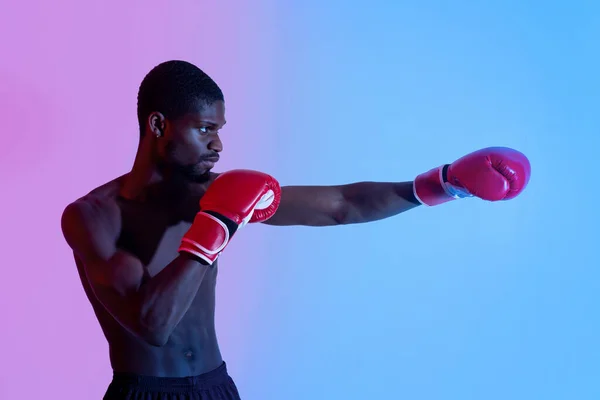 Seitenansicht des professionellen schwarzen Boxers in Handschuhen, der Schläge in Neonbeleuchtung wirft — Stockfoto