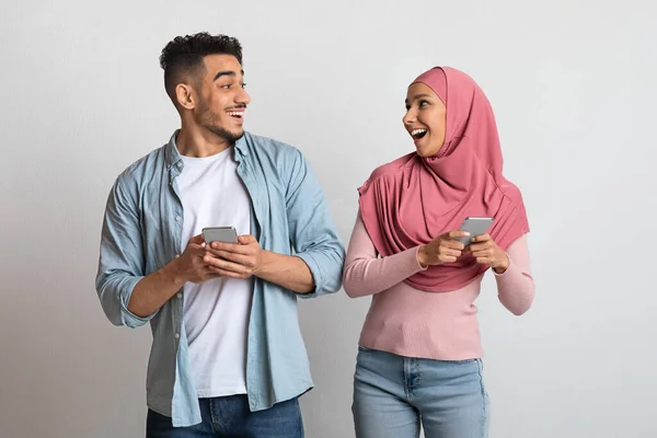 Online ajánlat. Izgatott iszlám pár kezében okostelefonok és nézik egymást — Stock Fotó