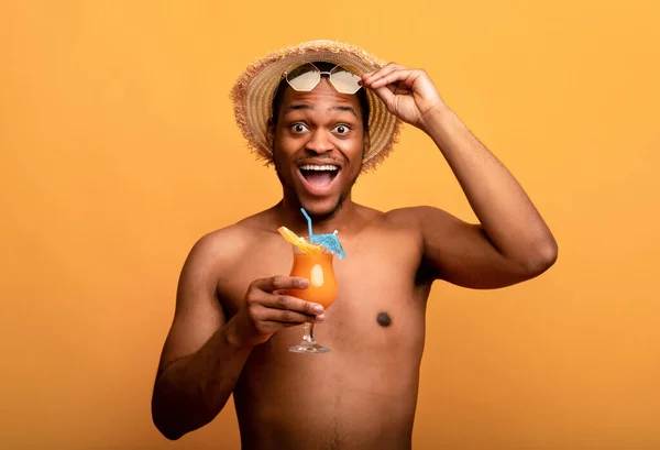 Excited black guy in straw hat and sunglasses having beach vacation, drinking tropical cocktail on yellow background