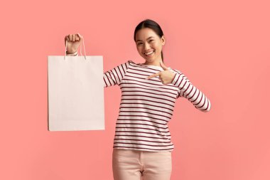 Satış ve Tüketim Konsepti. Boş alışveriş çantasına işaret eden mutlu Asyalı kadın,