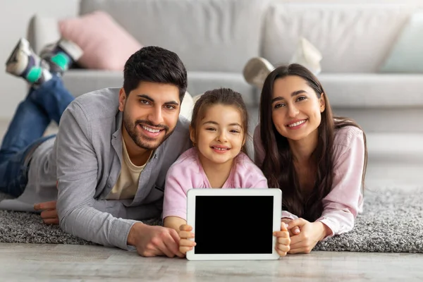 Família feliz de pais orientais e menina mostrando tablet digital com tela vazia para maquete — Fotografia de Stock