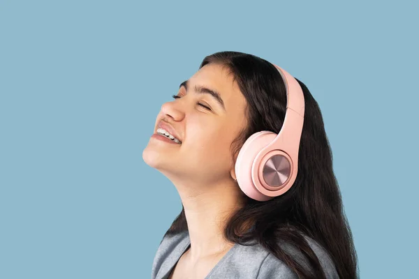 Amante da música. Calma indiana adolescente menina em fones de ouvido ouvindo bela música com olhos fechados no fundo azul — Fotografia de Stock