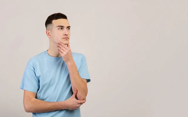 Joven pensativo pensando en el problema, tomando decisiones, mirando el espacio en blanco sobre fondo gris del estudio —  Fotos de Stock