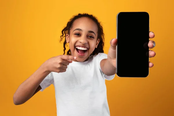 Чорна дівчина показує порожній екран смартфона і вказує — стокове фото