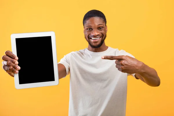 Позитивный африканский американец указывает на планшет с чистым черным экраном на желтом фоне, место для макета — стоковое фото