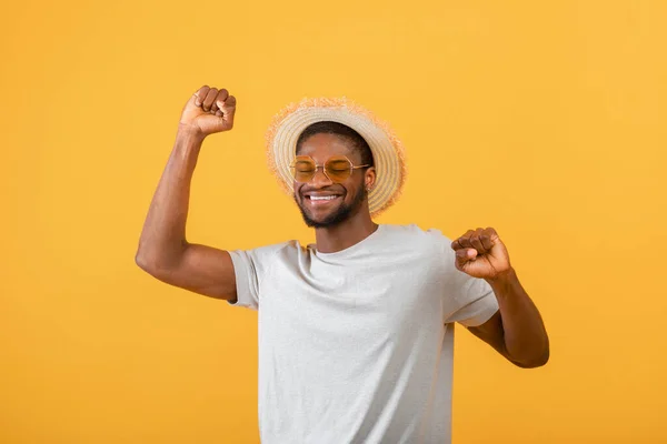 Alegre afroamericano chico en ropa casual, sombrero de paja y gafas de sol sobre fondo amarillento, toma de estudio — Foto de Stock