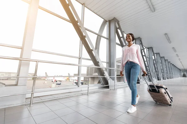 Mulher viajante afro-americana feliz andando com mala de bagagem no terminal do aeroporto — Fotografia de Stock