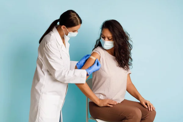 全科医生在蓝色背景下为年轻女性患者接种疫苗 — 图库照片