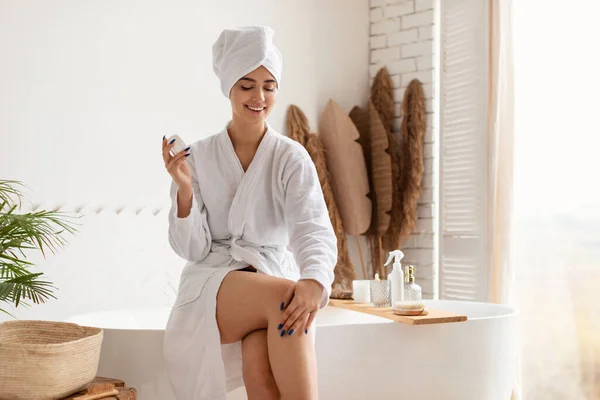 Mujer joven aplicando humectante en las piernas después de depilación en el baño —  Fotos de Stock