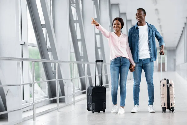 Las mejores aerolíneas. feliz negro pareja en aeropuerto apuntando lejos en copia espacio — Foto de Stock