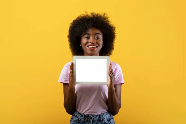 Alegre señora afroamericana sosteniendo tableta digital con pantalla en blanco sobre fondo amarillo — Foto de Stock